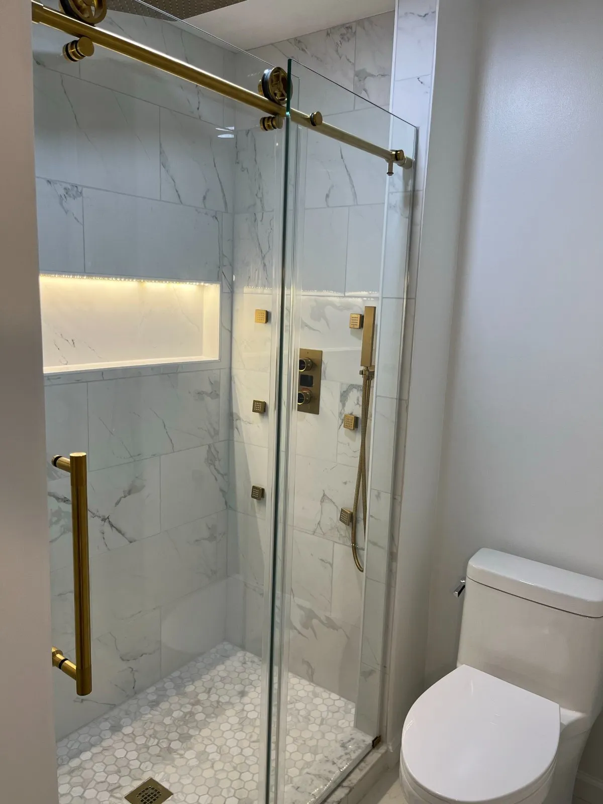 Finished walk-in shower with gold fixtures and a hex tile floor