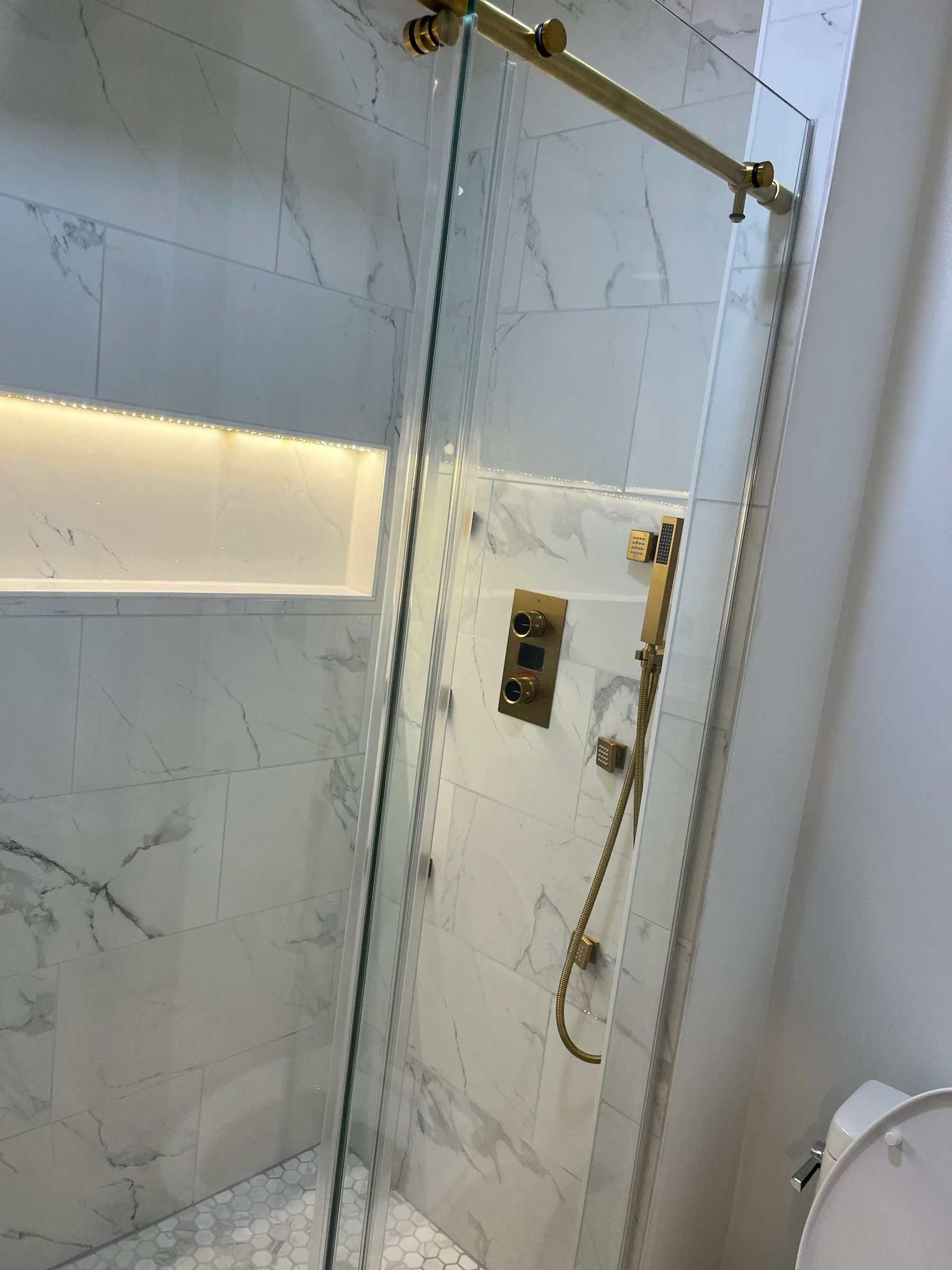 Finished tile shower with marble-look walls, a glass door and gold fixtures