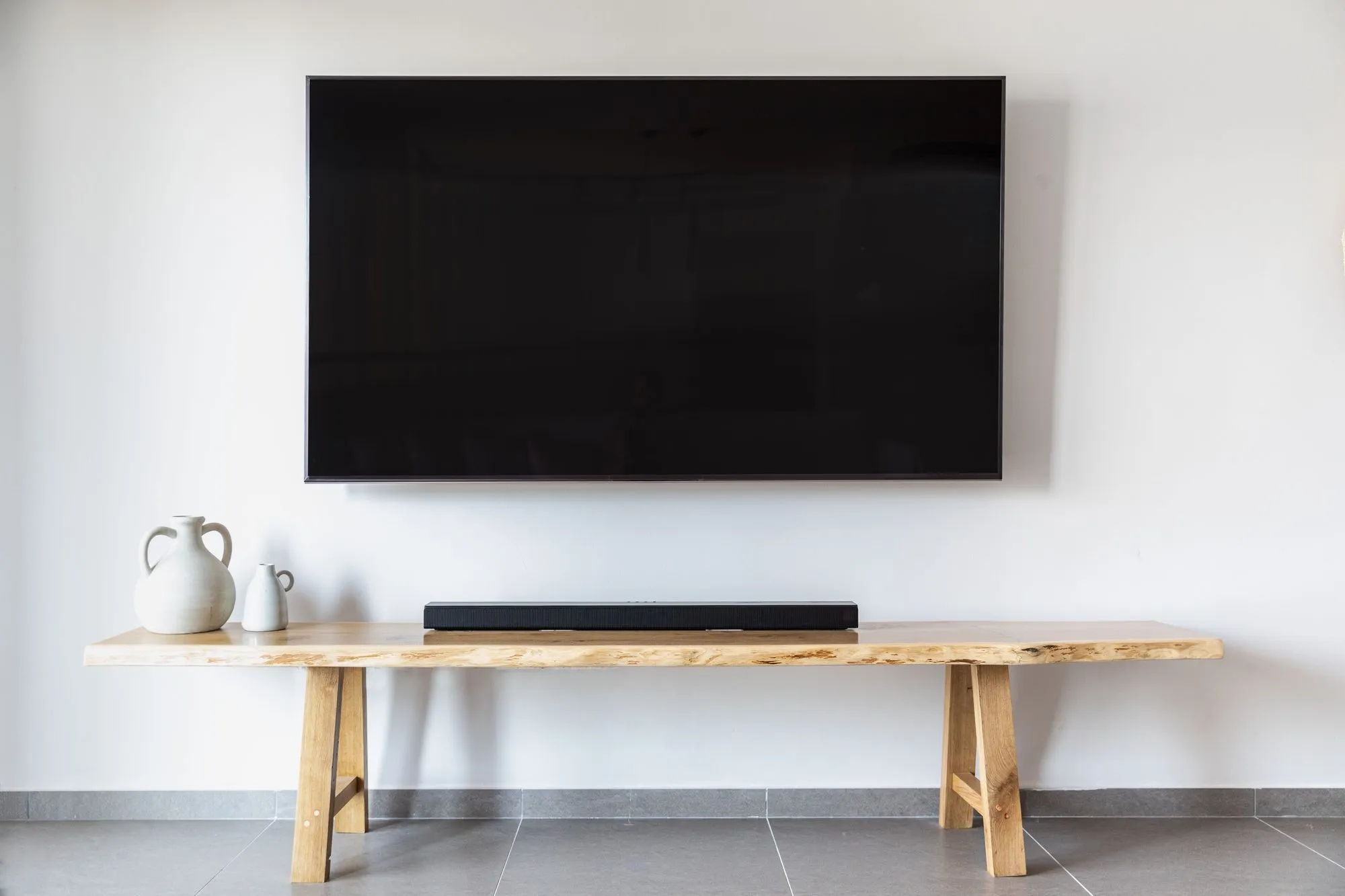 Flat-screen TV mounted on a white wall above a wood bench